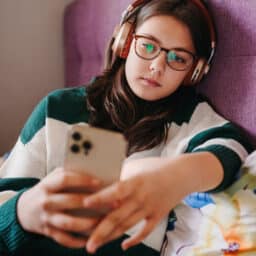 Kid in bed wearing headphones using her phone