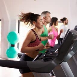 four people lined up using treadmills at the gym, the focus is on a middle-aged woman with hair flying behind her