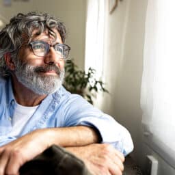 Smiling man looking out the window in his living room thoughtfully