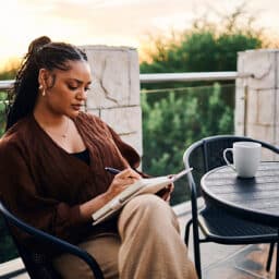 A woman sitting on her patio and writing in her journal in the morning