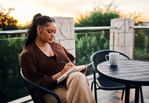A woman sitting on her patio and writing in her journal in the morning